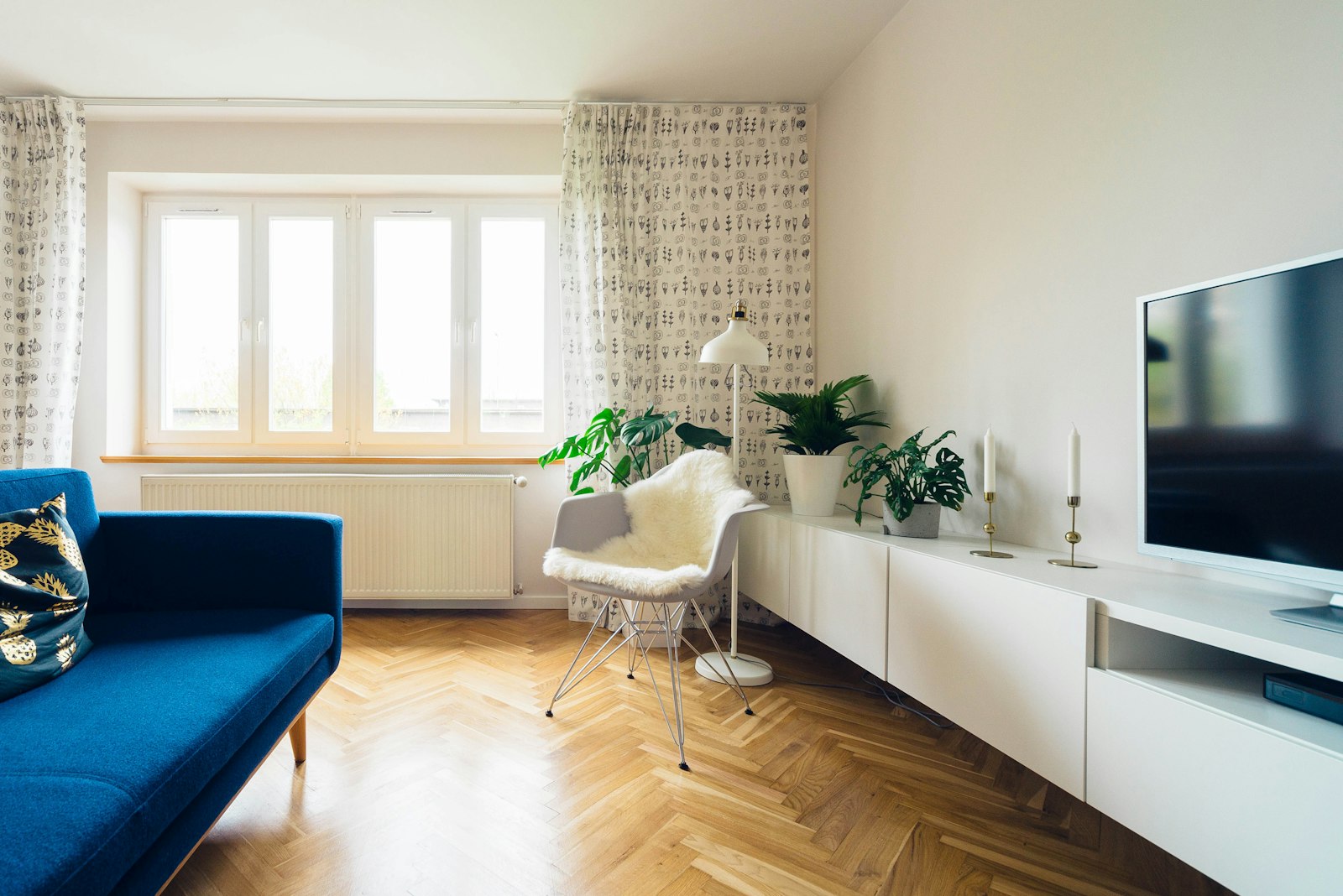 Lichte woonkamer met planten, een blauwe bank en een radiator onder het raam